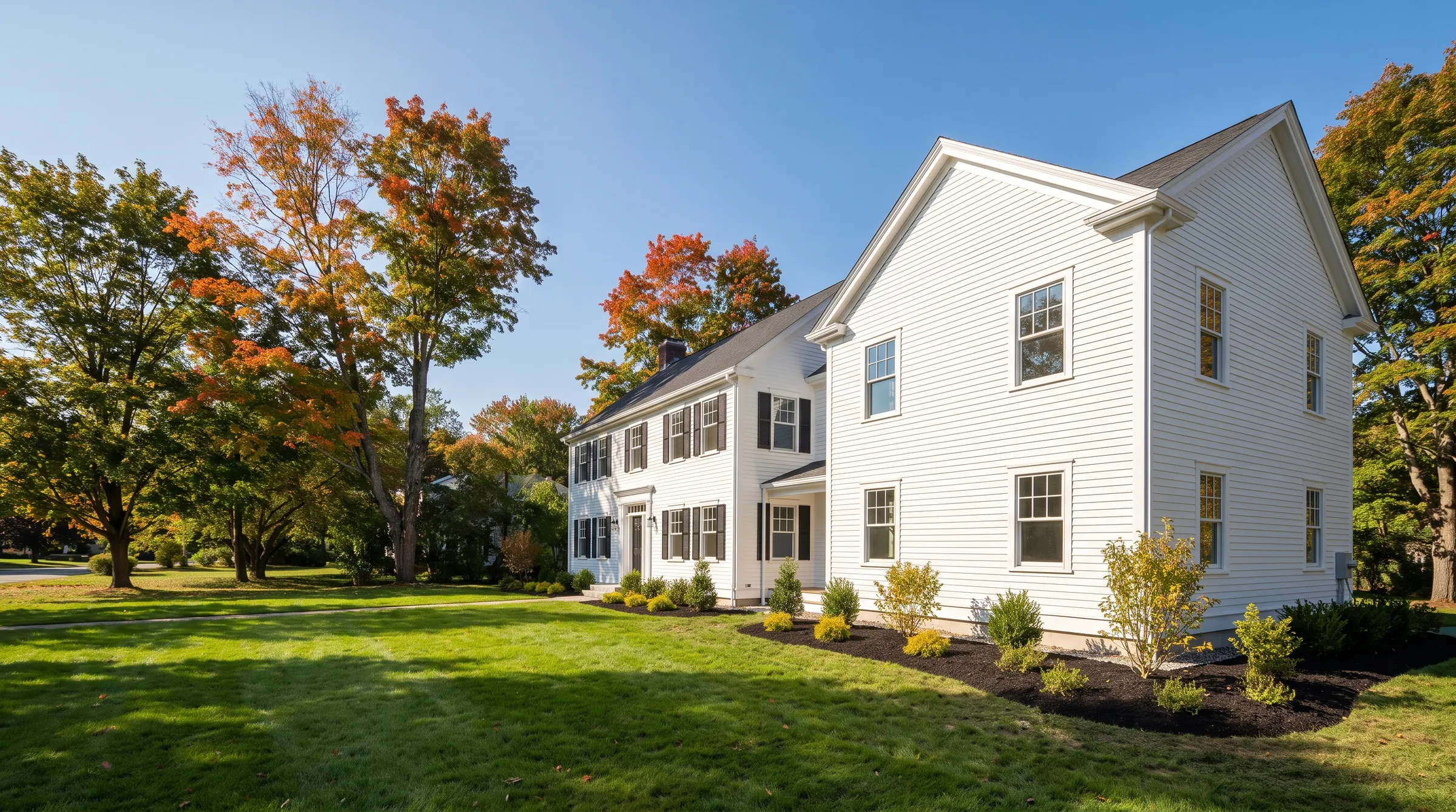 A white colonial with a large new front-gable addition, early October maples, blue sky
