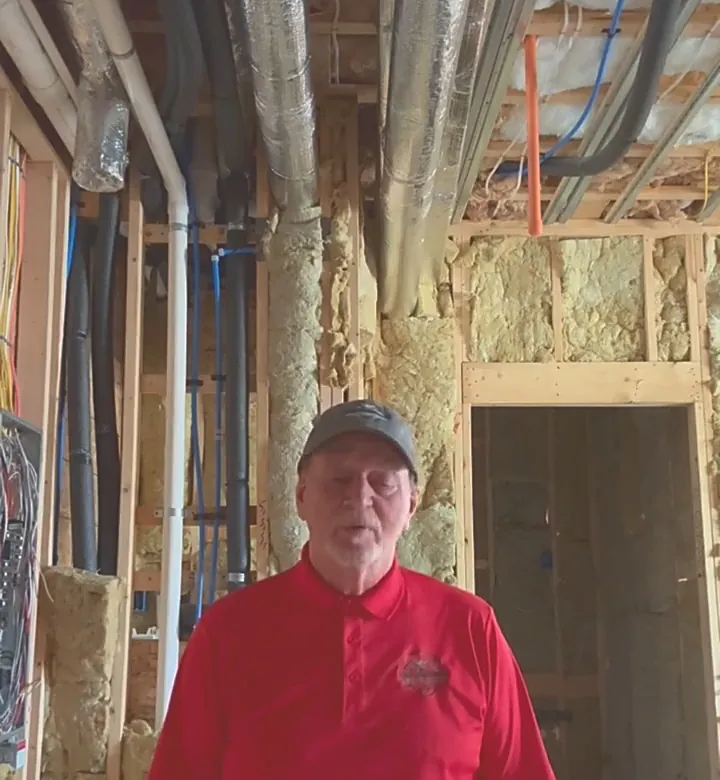 Stephen Selby in a basement under construction, ductwork, wiring and open framing overhead